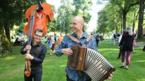 Ein Mann trägt einen Kontrabass über den Schultern, ein anderer spielt Akkordeon.