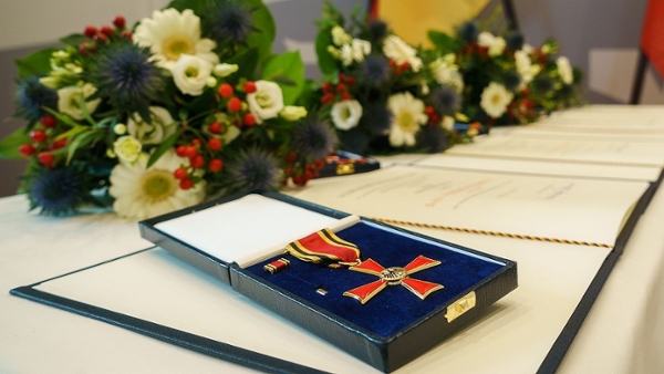 Auf einem mit Blumen geschmückten Tisch liegen ein Bundesverdienstkreuz in einer blauen Schatulle auf der dazugehörigen Urkunde.