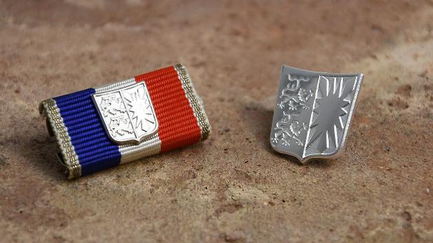 Silberner Anstecker mit eingeprägtem schleswig-holsteinischem Landeswappen sowie eine Bandschnalle, bezogen mit blau-weiß-rotem Band und einem silbernen Landeswappen. (Quelle: Staatskanzlei) Silberner Anstecker mit eingeprägtem schleswig-holsteinischem Landeswappen sowie eine Bandschnalle, bezogen mit blau-weiß-rotem Band und einem silbernen Landeswappen.