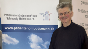 Ein Mann steht neben einem Plakat der Patientenombudsleute Schleswig-Holstein
