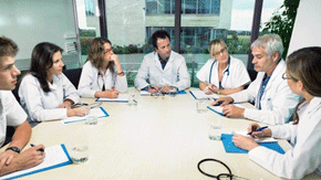 Ärzte sitzen in einer Runde am Tisch und haben Akten vor sich liegen.