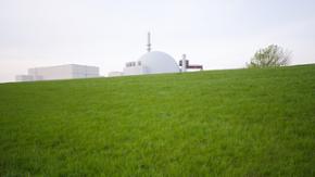 Zu sehen ist eine grüne Wiese, hinter der das Atomkraftwerk Brokdorf in den Himmel ragt.