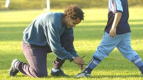 Ehrenamtlicher Fußballtrainer bindet einem Jungen die Schuhe