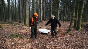 Zwei Jäger demonstrieren den sicheren Abtransport von Schwarzwild mit Hilfe von Sack und Wildschlitten, im Seuchenfall ist zusätzlich Schutzkleidung erforderlich.