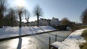 Angefrorene Gracht mit Brücke und historischer Häuserzeile, verschneit