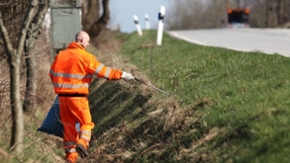 Ein Straßenwart sammelt Müll am Straßenrand.