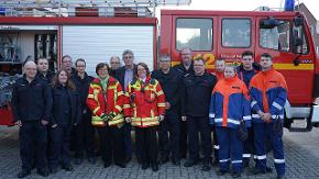 Vor einem Feuerwehrauto stehen viele Menschen.