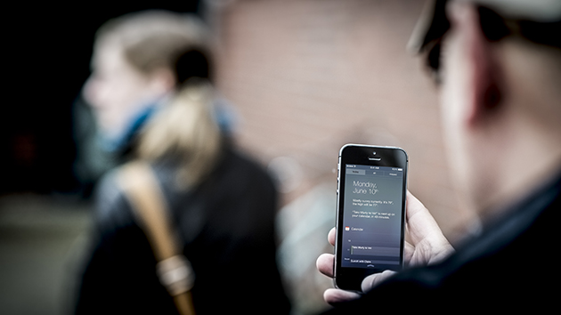 Bild zeigt eine Person mit einem Handy in der Hand, im Hintergrund geht eine Frau nach links