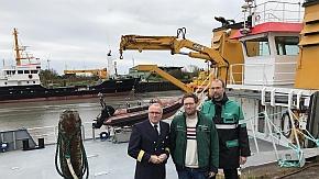 Drei Männer stehen vor einem Hafen mit Schiffen.