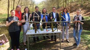 Eine Gruppe Menschen hält einen langen Ast in der Hand, von dem aus Holz und Moos gebastelte Buchstaben abstehen. Zusammen bilden sie das Wort "Naturerlebnis".