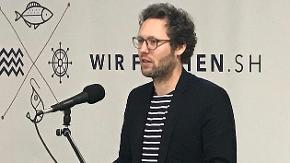 Ein Mann steht an einem Rednerpult und spricht in ein Mikrofon. 