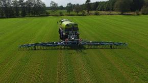 Über ein grünes Feld fährt ein Traktor, der mit seinem Gerät Gärreste verteilt. 