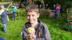 Ein Junge hält einen frisch geernteten Apfel in die Kamera