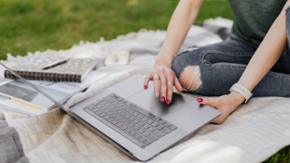 Eine Frau nutz ihren Laptop auf einer Decke im Park.