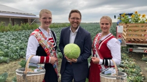 Landwirtschaftsminister Jan Philipp Albrecht mit einem Weißkohlkopf in den Händen. Er steht zwischen zwei Frauen, die Trachten tragen.