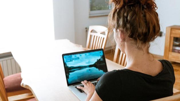 Eine junge Frau sitzt am leeren Küchentisch vor einem Laptop