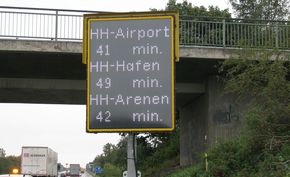 LED-Anzeigentafel mit Zielen und Zeitangaben vor einer Autobahnbrücke