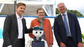 Zwei Männer und eine Frau stehen hinter einem kleinen Roboter.