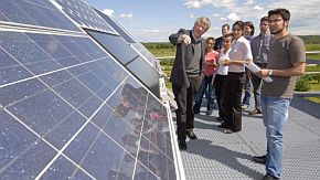 Mehrere Menschen stehen auf einem Dach und betrachten eine Solaranlage.