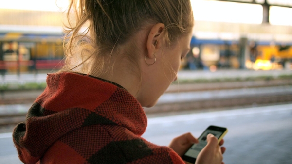 Eine Junge Frau steht am Bahnhof und schaut auf ihr Smartphone