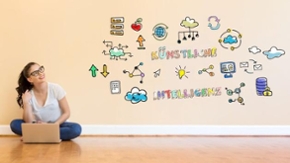 Eine junge Frau sitzt vor einer Wand mit bunten Symbolen. In bunten Buchstaben sind die Worte Künstliche Intelligenz an die Wand geschrieben.