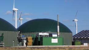 Zwei große Hallen mit Kuppeldächern und Geräte zur Stromerzeugung. Im Hintergrund stehen Windräder.