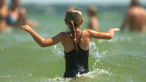Ein Mädchen im Wasser, im Hintergrund Badegäste