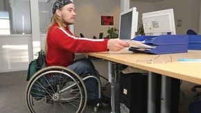 Rollstuhlfahrer arbeitet im Büro am Computer.