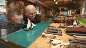 Ein Junge und ein älterer Mann stehen vor einer Vitrine und schauen sich darin das Modell einer Schiffswerft an.