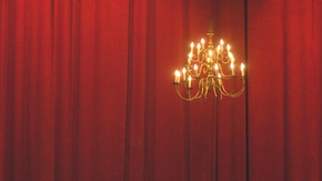 Goldener Kronleuchter vor einem roten Theatervorhang