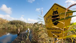 Ein Schild mit der Aufschrift 'Naturschutzgebiet', im Hintergrund ein Gewässer.