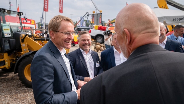 Ministerpräsident Günther steht auf dem Außengelände der Nordbau-Messe vor einem Bagger. Er unterhält sich mit mehreren Männern und lacht dabei. (Quelle: Staatskanzlei) Ministerpräsident Günther steht auf dem Außengelände der Nordbau-Messe vor einem Bagger. Er unterhält sich mit mehreren Männern und lacht dabei.