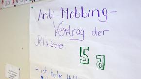 Ein Zettel mit der Aufschrift "Anti-Mobbing-Vertrag der Klasse 5a" hängt an einer Klassenzimmerwand.