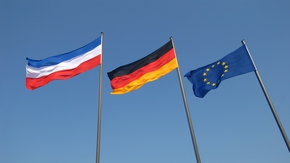 Vor blauem Himmel wehen die Flaggen von Schleswig-Holstein, Deutschland und Europa