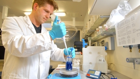 Im Labor entnimmt ein Forscher mit einer Pipette blaue Flüssigkeit aus einem Behälter