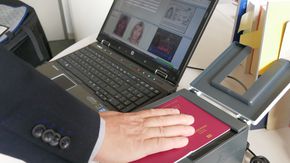 Eine Person prüft auf dem Gerät, an dem ein Laptop angeschlossen ist, einen Reisepass
