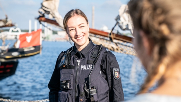 Eine junge Polizistin steht in einem Hafen und lächelt in die Kamera