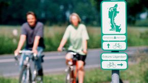 Zwei Radfahrer fahren an einem Schild vorbei, dass auf den Ochsenweg verweist.