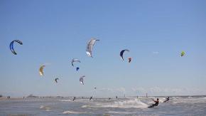 Bunte Kitesurf-Schirme und Kiter vor blauem Himmel nahe des Strandes