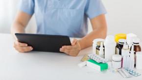 Eine Person sitzt an einem Tisch, auf dem Medikamente liegen und hat ein Tablet in der Hand (Quelle: adpic.de) Eine Person sitzt an einem Tisch, auf dem Medikamente liegen und hat ein Tablet in der Hand