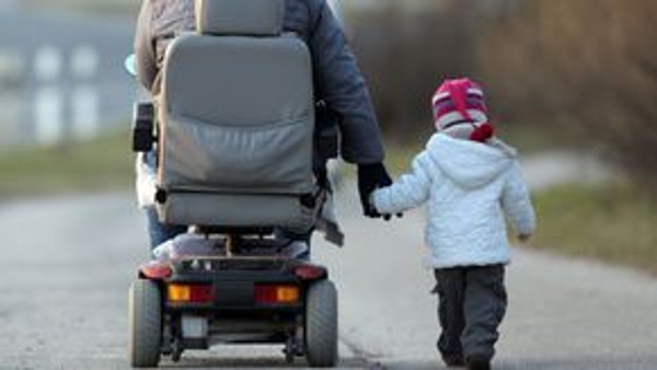 Ein Kind läuft Hand in Hand mit einem Mann im Rollstuhl über eine Straße